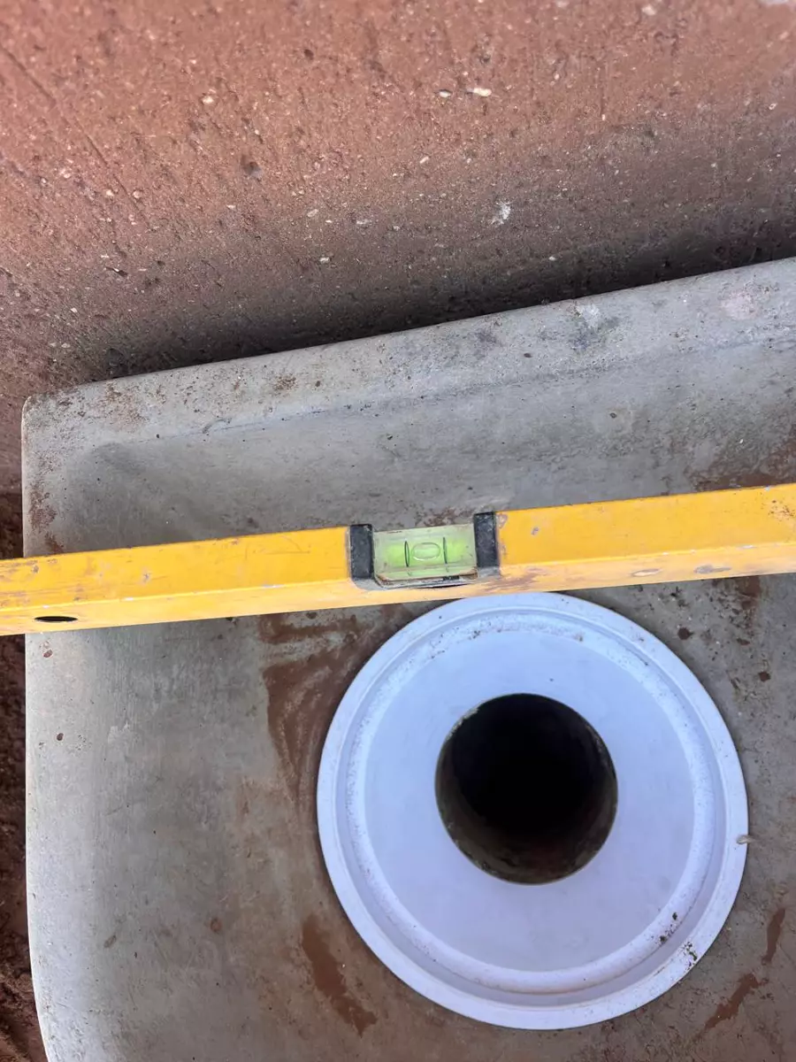 Yellow spirit level placed across a concrete drain basin with a white plastic drain opening